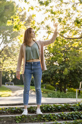 Young redheaded woman touching leave in a park - AFVF03171