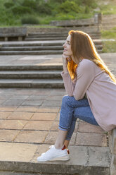Junge rothaarige Frau sitzt in einem Park - AFVF03189