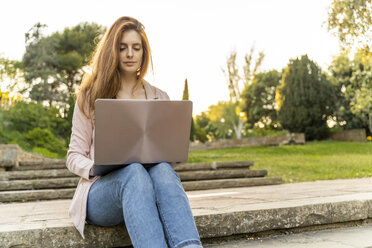 Young redheaded woman using laptop, sitting on steps in a park - AFVF03190