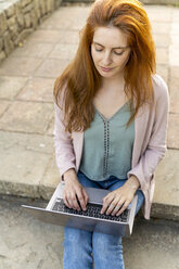 Junge rothaarige Frau mit Laptop, auf Stufen in einem Park sitzend - AFVF03191