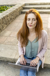 Young redheaded woman using laptop, sitting on steps in a park - AFVF03192