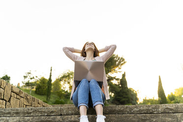 Young redheaded woman using laptop, sitting on steps in a park - AFVF03193