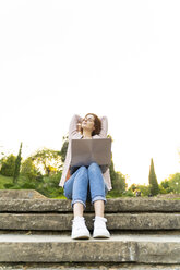 Junge rothaarige Frau mit Laptop, auf Stufen in einem Park sitzend - AFVF03197