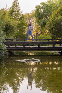 Junge rothaarige Frau steht auf dem Geländer einer Brücke in einem Park - AFVF03208