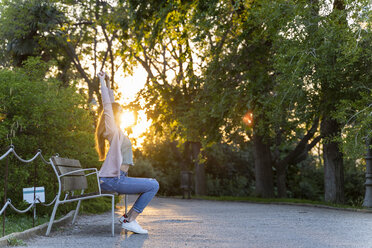 Young redheaded woman stretching arms on a bank in a park - AFVF03212