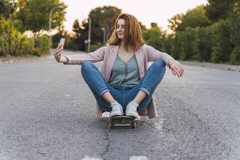 Junge Frau auf Skateboard und macht ein Selfie, lizenzfreies Stockfoto