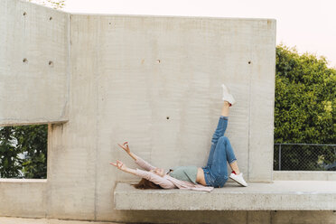 Young redheaded woman with raised arms lying on concrete bench - AFVF03226