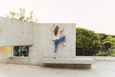 Young redheaded woman with raised arm on concrete bench - AFVF03227