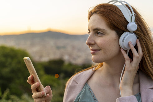 Junge rothaarige Frau mit Kopfhörern und Smartphone auf Aussichtspunkt - AFVF03234