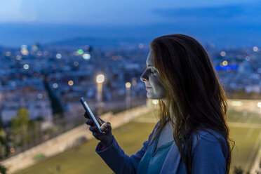 Junge Frau mit Smartphone an einem Aussichtspunkt zur blauen Stunde, Barcelona, Spanien - AFVF03235