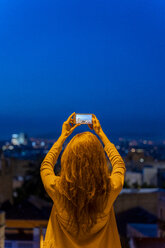 Junge Frau mit Smartphone an einem Aussichtspunkt zur blauen Stunde, Barcelona, Spanien - AFVF03243