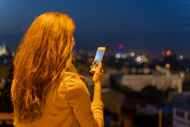 Junge Frau mit Smartphone an einem Aussichtspunkt zur blauen Stunde, Barcelona, Spanien - AFVF03244