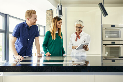 Verkäuferin mit Tablet im Gespräch mit einem Paar, das eine neue Küche im Ausstellungsraum kauft, lizenzfreies Stockfoto