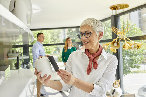 Ältere Frau betrachtet eine Vase in einem Ausstellungsraum, lizenzfreies Stockfoto