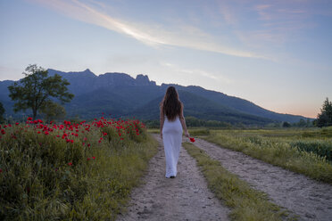 Rückansicht einer eleganten jungen Frau, die eine Mohnblume auf dem Lande hält, Garrotxa, Spanien - AFVF03248