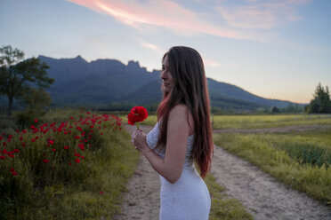 Elegante junge Frau hält eine Mohnblume in der Landschaft, Garrotxa, Spanien - AFVF03249