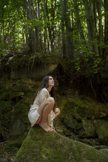 Junge Frau sitzt auf einem Felsen im Wald, Garrotxa, Spanien - AFVF03256