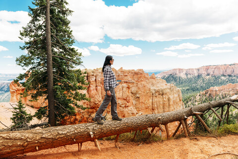 Reisende Frau, die auf dem Stamm eines umgestürzten Baumes spaziert und die Aussicht im Bryce Canyon, Utah, USA, genießt, lizenzfreies Stockfoto