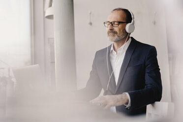 Mature businessman with closed eyes listening to music with headphones - KNSF05900