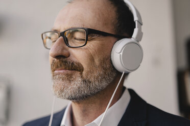 Älterer Geschäftsmann mit geschlossenen Augen, der mit Kopfhörern Musik hört - KNSF05901