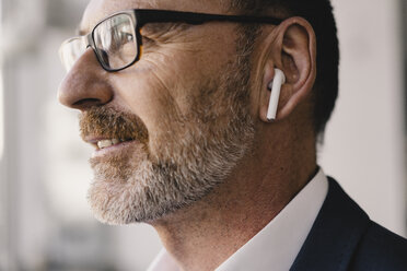 Portrait of mature businessman listening to music with bluetooth earbuds - KNSF05907