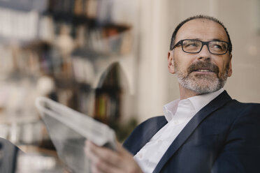 Reifer Geschäftsmann, der eine Zeitung hält und zur Seite schaut - KNSF05910