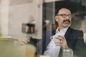 Älterer Geschäftsmann sitzt in einem Café und schaut zur Seite - KNSF05911