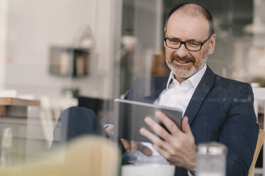 Smiling mature businessman using tablet in a cafe - KNSF05915