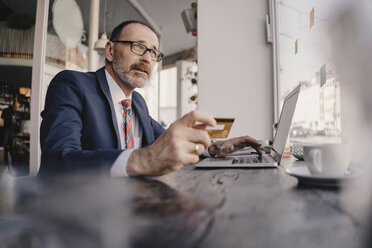 Älterer Geschäftsmann mit Laptop und Kreditkarte in einem Cafe - KNSF05932