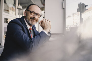 Portrait of smiling mature businessman in a cafe - KNSF05933