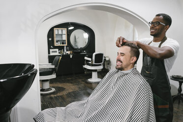 Lächelnder Friseur, der einem Kunden im Friseursalon die Haare schneidet - AHSF00494