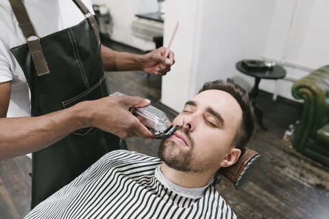 Barbier schneidet Bart eines Kunden im Friseursalon, lizenzfreies Stockfoto