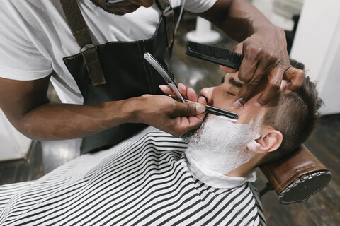 Mann, der seinen Bart mit einem Rasiermesser im Friseursalon rasiert bekommt, lizenzfreies Stockfoto