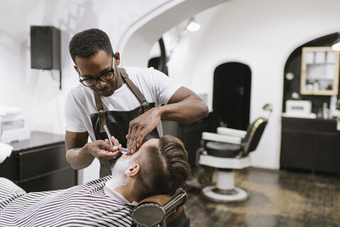 Mann, der seinen Bart mit einem Rasiermesser im Friseursalon rasiert bekommt, lizenzfreies Stockfoto