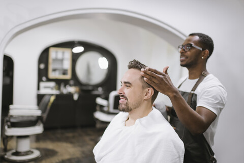 Lächelnder Friseur, der den Haarschnitt eines Kunden in einem Friseursalon beendet, lizenzfreies Stockfoto