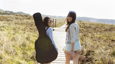 Zwei glückliche Frauen mit Gitarrentasche auf der Strandpromenade in den Dünen - MGOF04050