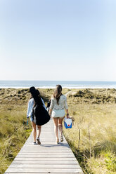 Rear view of women with guitar bag walking in dunes towards beach - MGOF04051