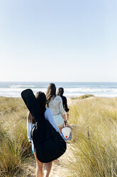 Rückansicht einer Frau mit Gitarrentasche, die in den Dünen in Richtung Strand läuft - MGOF04052