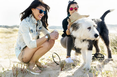 Zwei glückliche Frauen mit Hund am Strand - MGOF04054