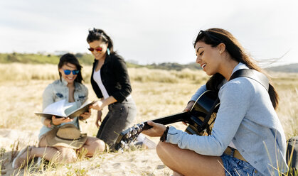 Junge Frau mit Freunden spielt Gitarre am Strand - MGOF04056