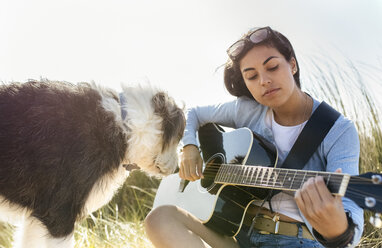 Junge Frau mit Hund spielt Gitarre am Strand - MGOF04057