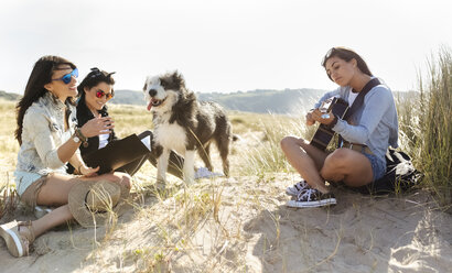 Drei glückliche Frauen mit Hund und Gitarre am Strand - MGOF04058