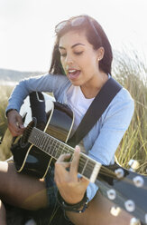 Junge Frau singt und spielt Gitarre am Strand - MGOF04061