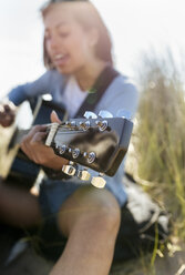 Nahaufnahme einer jungen Frau, die am Strand singt und Gitarre spielt - MGOF04062