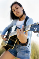 Nahaufnahme einer jungen Frau, die am Strand Gitarre spielt - MGOF04064