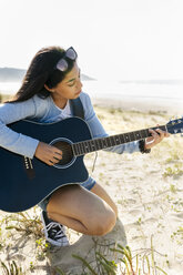 Junge Frau spielt Gitarre am Strand - MGOF04065