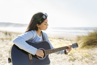 Junge Frau spielt Gitarre am Strand - MGOF04066