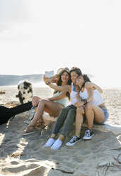 Glückliche Freundinnen mit Hund machen ein Selfie am Strand - MGOF04072