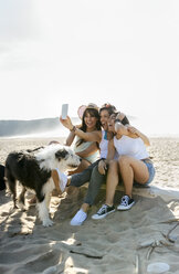 Glückliche Freundinnen mit Hund machen ein Selfie am Strand - MGOF04073