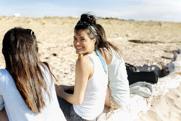 Glückliche Freundinnen sitzen auf einem Baumstamm am Strand - MGOF04078